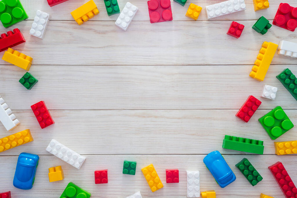 Kleurrijke plastic bouwblokken op witte houten achtergrond als kinderspeelgoed frame met kopieerruimte voor tekst. Plat gelegd. Bovenaanzicht. - Foto, afbeelding