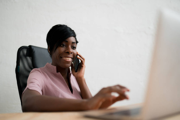 A woman sits at a table and looks at a computer while making a phone call. Work remotely - Fotó, kép