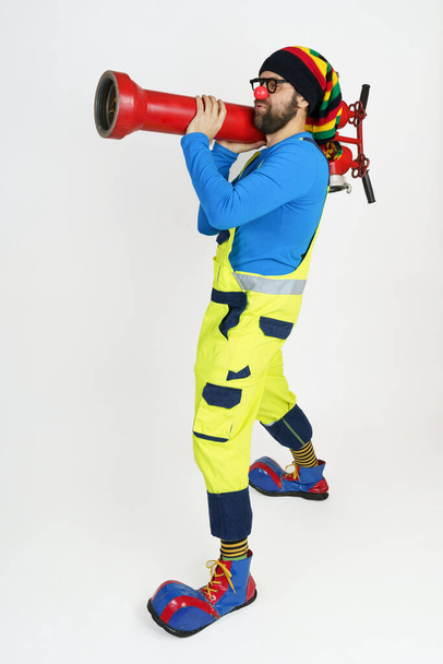 Holiday and fun concept. The clown firefighter holds a fire pump in his hands like a grenade launcher. - Фото, зображення