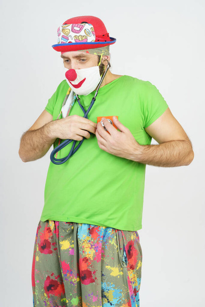 Holiday and fun concept. The clown plays doctor, listens to his heart with a stethoscope. Isolated on white - Foto, Imagem