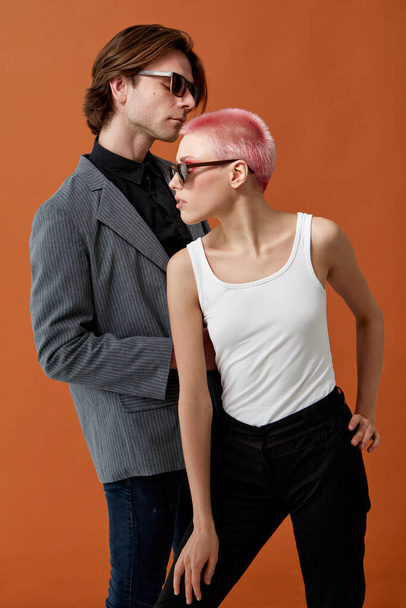 Elegante joven hipsters sexy mujer con el pelo corto rosa y el hombre en gafas de sol, posando juntos, sobre fondo marrón. Vista vertical. - Foto, Imagen