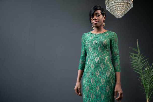 African American woman stands in the center of the hall on a dark background in a beautiful long green dress - Foto, immagini