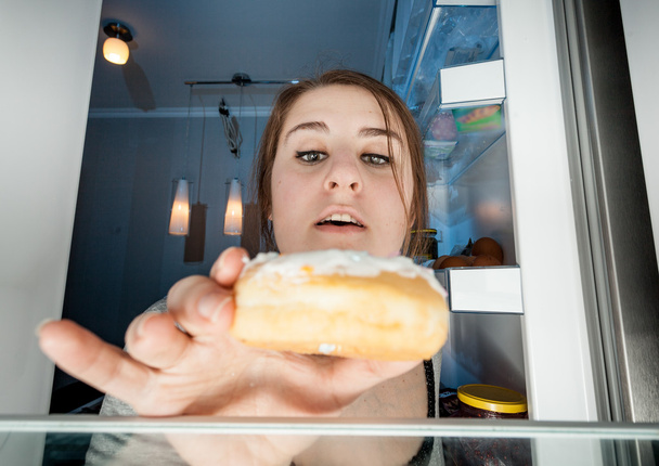 Portrait of woman taking donut from fridge - Photo, Image