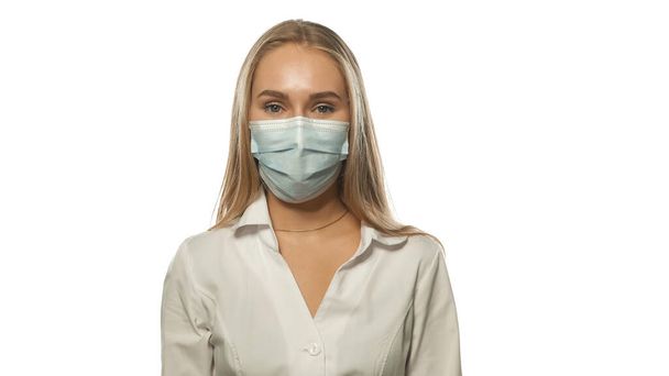 Charing blond haired nurse in a medical mask and white uniform looking at the camera. Isolated on white background - Photo, image