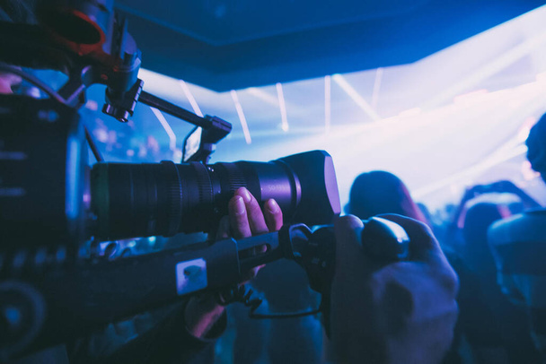 Kameramann mit Kamera in der Hand am Set. Professioneller Videofilmer bei der Arbeit an Film-, Werbe- oder Fernsehserien. Die Dreharbeiten im Innenraum, auf einer Konzertbühne mit Neonlicht. - Foto, Bild