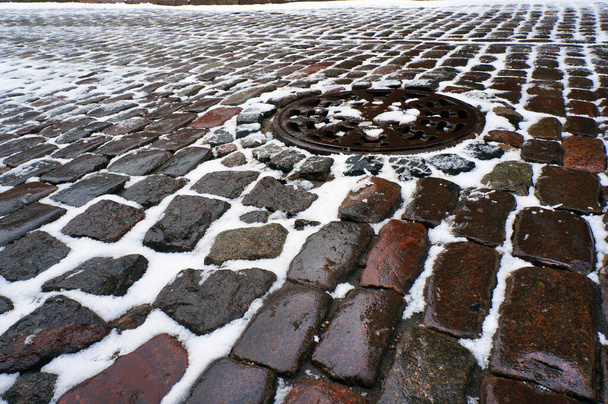 Stare tradycyjne bruk kamienny i pokrywa włazu pokryte śniegiem w zimie.                                  - Zdjęcie, obraz
