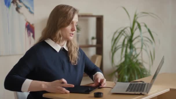 Medium laukaus nuori naisartisti opettaa, miten hyödyntää digitaalista piirustus pöytä ottaa online-oppitunnin kautta kannettava istuu työpöydän sisällä - Materiaali, video