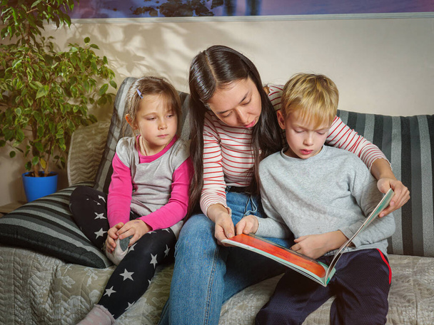 Kindermädchen liest Kindern ein Buch vor. Die Arbeit mit Kindern zu Hause. Bildung und Zeitvertreib mit Kindern - Foto, Bild
