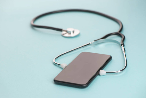 Close-up on a phone with a stethoscope on blue background - Foto, afbeelding