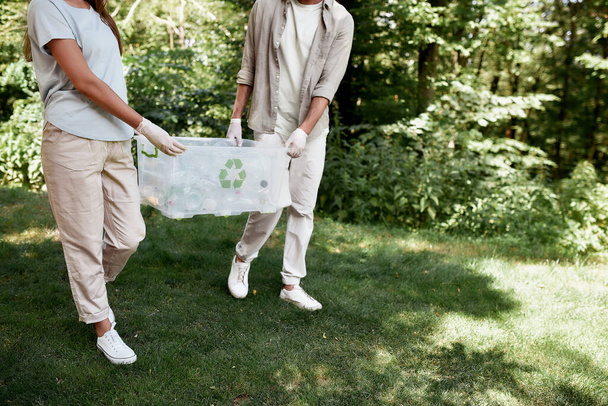Plastic pollution. Cropped shot of two volunteers carrying recycle bin, collecting plastic waste together in the forest or park - Фото, зображення