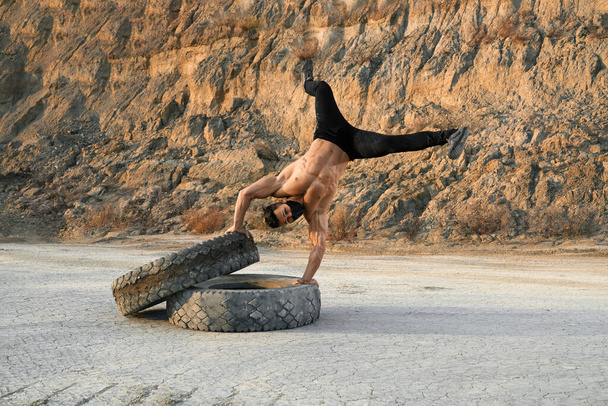 Fitness man standing on hands on tires outdoor - Фото, зображення