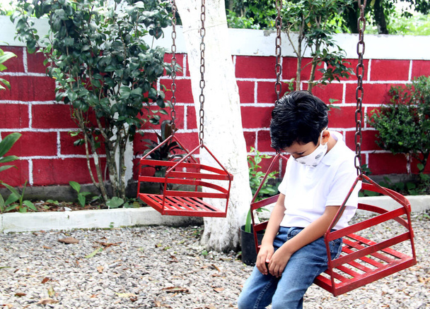 6-jähriger Latino-Junge mit Covid-19-Schutzmaske, auf Schaukel, neue Normalität in Parks - Foto, Bild