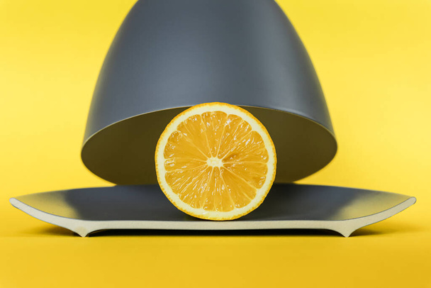 Μισό κίτρινο λεμόνι κάτω από το καπό σε γκρι πιάτο σε κίτρινο φόντο - Φωτογραφία, εικόνα