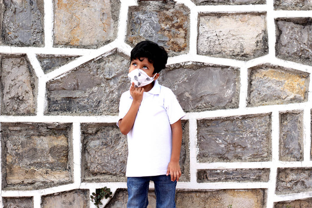 6-year-old latin boy with covid-19 protection mask, on stone wall background, new normal - Photo, Image