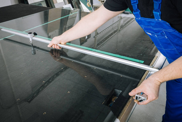 Le vitrier coupe le verre avec un traîneau de coupe sur une table professionnelle sur le lieu de travail - Photo, image
