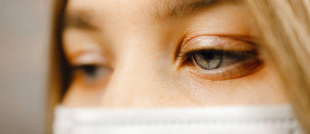 Vue macro-oculaire : Jeune infirmière aux yeux bleus portant un masque médical et regardant vers le bas - Photo, image
