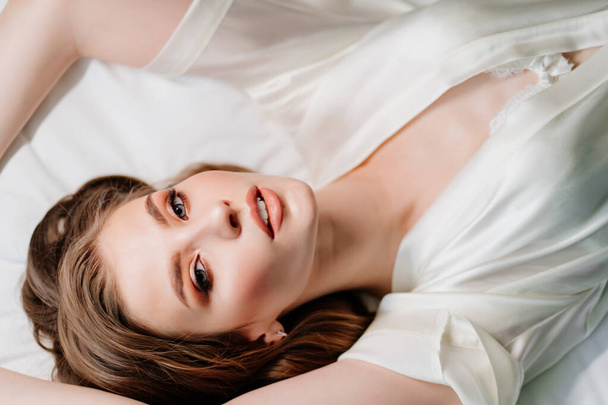 vista de cima. mulher sexy com maquiagem, cabelos longos encontra-se em roupão branco na cama - Foto, Imagem