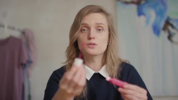 punkt zbliżenie młody kaukaski makijaż artysta trzymając jasnoróżowy szminka pokazując pędzel i rozmawiając jak dla stosować to patrząc w kamera - Materiał filmowy, wideo