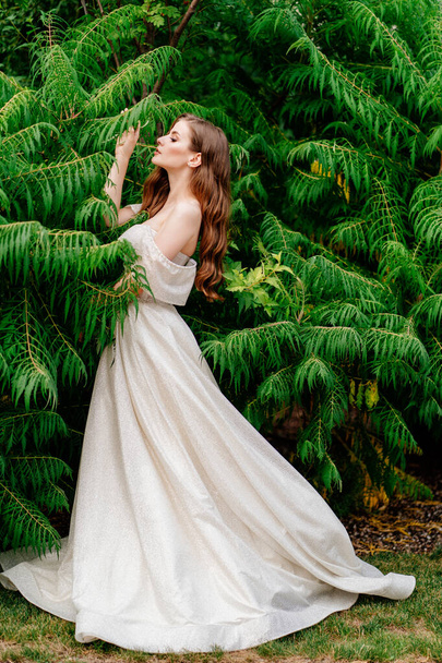 hermosa mujer en un vestido blanco posando en contra de hojas verdes. - Foto, imagen
