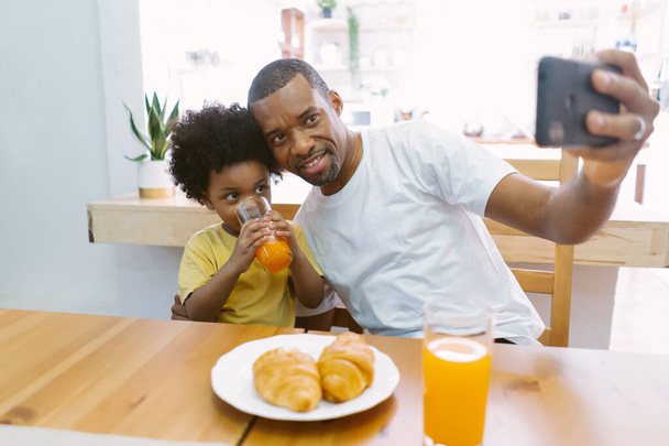 Happy smiling African American family  taking selfie by smartphone while eating breakfast on the table at home together. Family enjoy meal. Happy Father day. - Фото, зображення