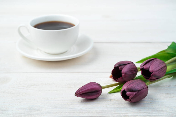 Tulipes violettes et une tasse de café blanche en arrière-plan sur un fond en bois clair. - Photo, image