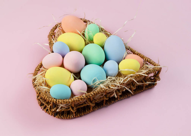 Pastel multi-colored Easter eggs in a basket in the shape of a heart on a pink background. Top view, place for text. Greeting card. - Фото, зображення