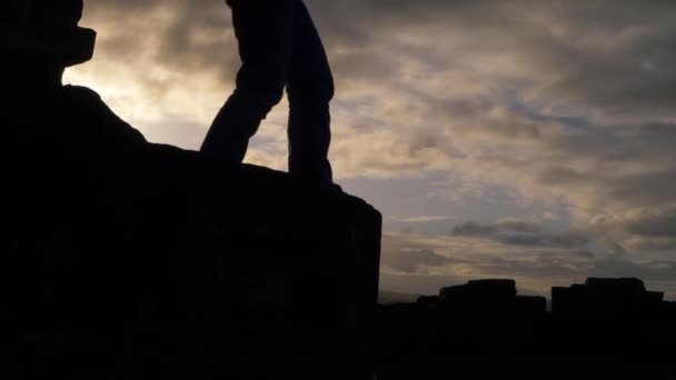 Kobieta wspinająca się na skały przed chmurnym niebem - Materiał filmowy, wideo