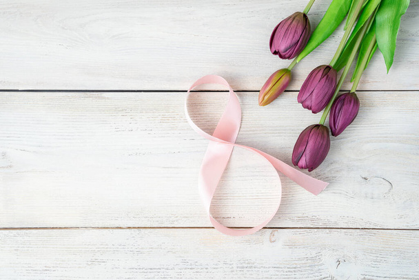 Kytice fialových tulipánů a růžové číslo 8 ze stužky na lehkém dřevěném pozadí. - Fotografie, Obrázek