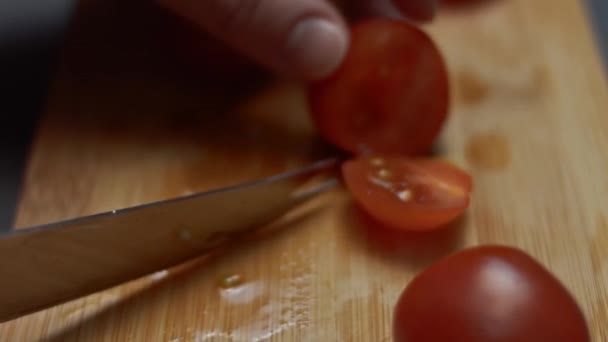 Las manos femeninas cortan los tomates cherry por la mitad con un cuchillo en una tabla de cortar de madera. Unir dos mitades de tomates cherry con un pincho de madera. Vídeo 4K - Imágenes, Vídeo