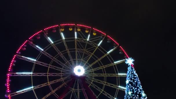 Ferris kerék pörgés és karácsony Újév fa közeli kilátás Kharkiv belvárosában park éjszaka színes fényes megvilágítás. Szezonális ünnepek dekoráció - Felvétel, videó
