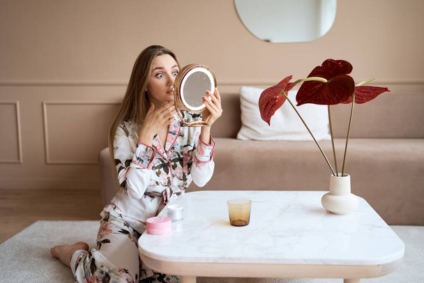 Attractive woman in pajamas applying face cream. Attractive young woman in pajama applying moisturizing cream on face. Fresh from the morning - Photo, image