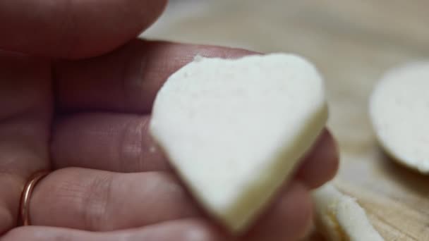 Γυναικείο χέρι που κρατά ένα σχήμα καρδιάς από τυρί μοτσαρέλα σε ξύλινο φόντο πίνακα κοπής. Ετοιμάζω φαγητό για την Ημέρα του Αγίου Βαλεντίνου. Βίντεο 4k - Πλάνα, βίντεο