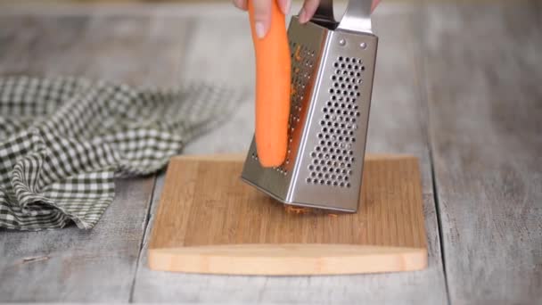 Manos femeninas rallando zanahoria en rallador de metal en una tabla de cortar. - Metraje, vídeo