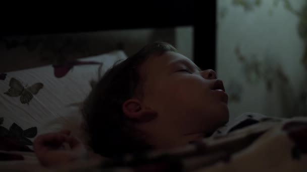 Расслабление, сладкие сны, детство, семейные конфузы - маленького 2-3-летнего дошкольника мокрый мальчик лежит на белой кровати, покрытой одеялом, в темной комнате во время ночного сна - Кадры, видео