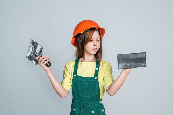lets start. renovation and repair. using working tool. teen girl in helmet and boilersuit with spatula. child wear hard hat. kid builder on construction site. worker engineer. architect in workshop - Foto, Bild