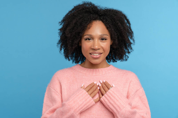 Romantická mladá afro-americká žena drží ruce na prsou, dívá se do kamery, usmívá se, má bílé zuby - Fotografie, Obrázek