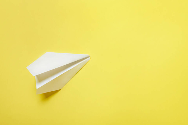 Een wit papieren vliegtuig geïsoleerd op een gele achtergrond. Vlakke lay, bovenaanzicht, kopieerruimte - Foto, afbeelding