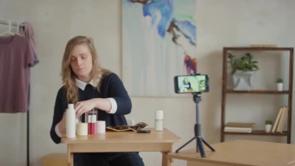 Cintura-up imagens de mulher caucasiana sentada na mesa de gravação de vídeo de como fazer maquiagem em casa escovas de lavagem usando água micelar - Filmagem, Vídeo