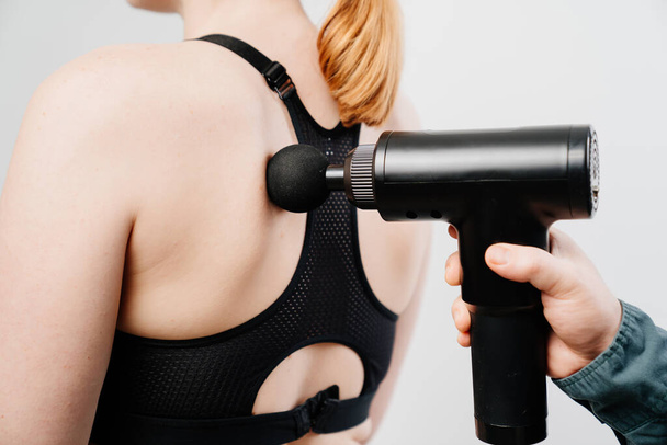 Een vrouw gebruikt een massagepistool. medische sportuitrusting.  - Foto, afbeelding