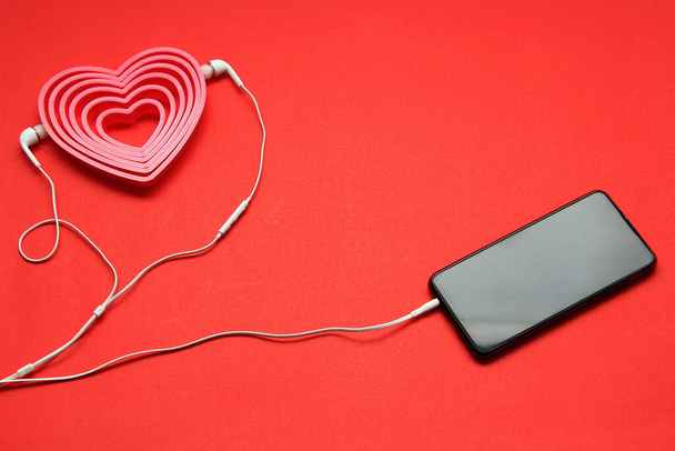 calling love, cell phone with headphones and pink hearts on red background, Valentine's day - Photo, Image