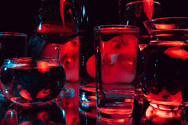 άνθρωπος κοιτάζοντας μέσα από γυάλινα ποτήρια του νερού με αντανακλάσεις και στρεβλώσεις - Φωτογραφία, εικόνα