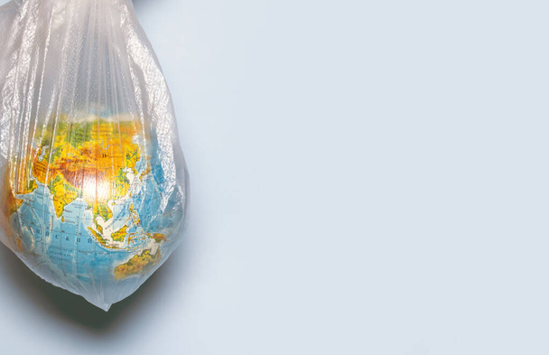 Ecology concept. Globe in plastic wrap on a blue background. Plastic waste environmental pollution concept. Place for text. - Photo, Image