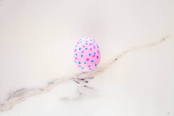  Cute Easter egg decorated by hand on a white table. Easter holiday concept. Beautiful egg speckled pink and blue. - Photo, Image