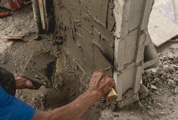 Un trabajador de la construcción o albañil alisa el hormigón húmedo colocado en la parte superior de una pared de CHB con una paleta. En un edificio comercial en construcción. - Foto, Imagen