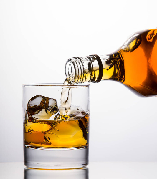 Pouring whisky from a bottle into a tumbler on white background - Photo, image