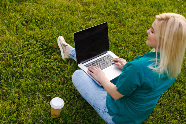 Vista dall'alto di donna seduta in parco sull'erba verde con computer portatile, mani sulla tastiera. Mockup dello schermo del computer. Studente che studia all'aperto. Copia spazio per testo - Foto, immagini
