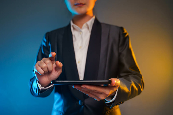 Een close-up van een zakenvrouw met een smartphone in een zwart pak. Elegante smart op zwarte achtergrond. - Foto, afbeelding