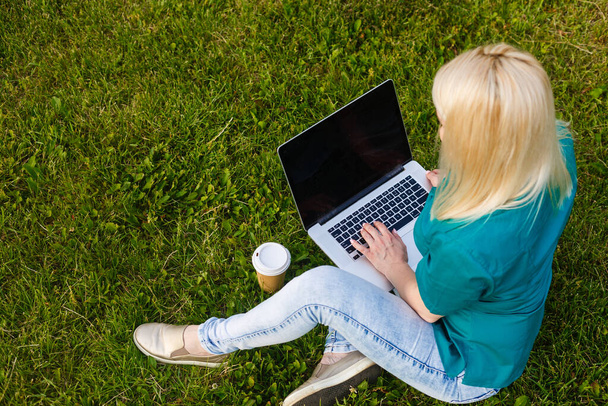 Bovenaanzicht van vrouw zittend in het park op het groene gras met laptop, handen op toetsenbord. Computerscherm model. Studenten studeren buiten. Kopieer ruimte voor tekst - Foto, afbeelding