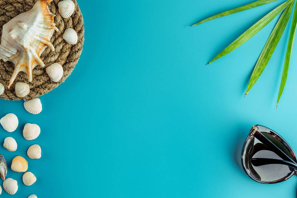 Eine Muschel auf einer Rutsche aus altem Seil, Sonnenbrille und Palmenzweig liegen auf aquamarinfarbenem Hintergrund. Tropenküsten-Urlaubskonzept - Foto, Bild