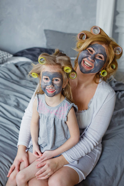 Gelukkige moeder en dochter met zwarte maskers in de slaapkamer op het bed. Het concept van home entertainment. - Foto, afbeelding
